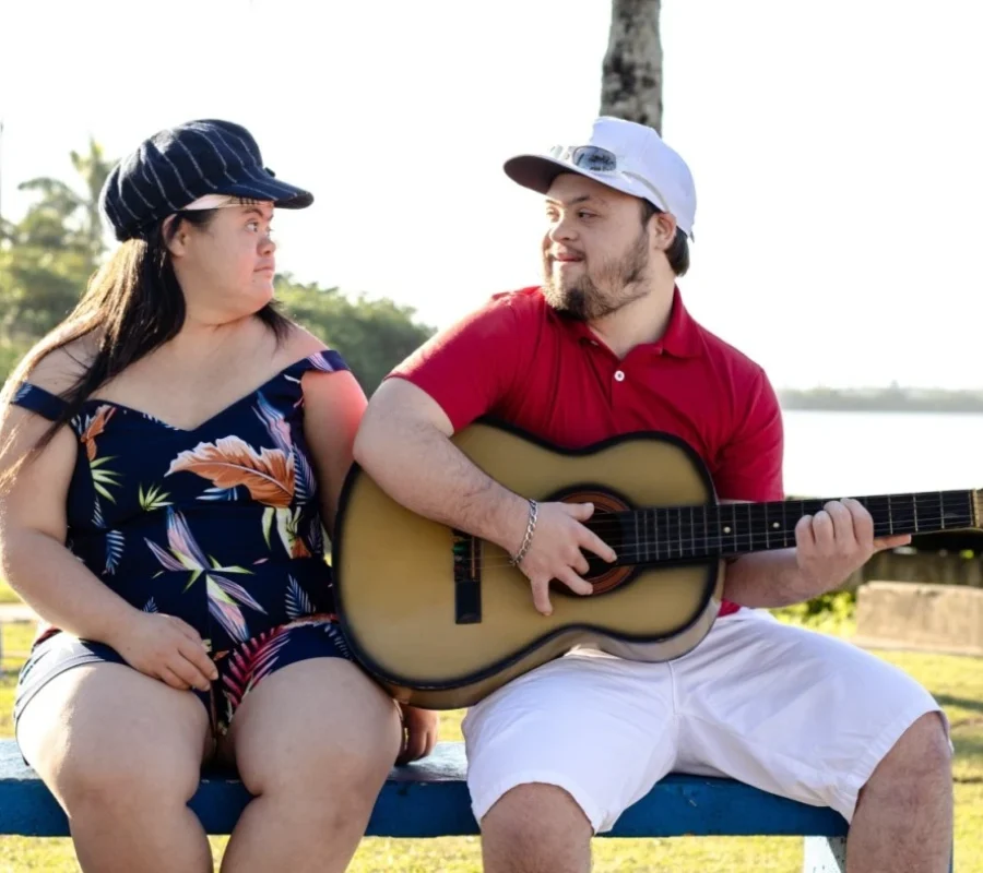 Two friends with down syndrome sitting together on park bench playing guitar